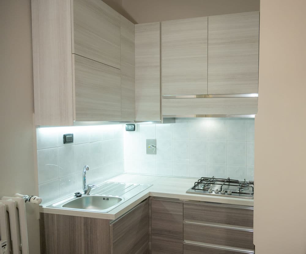 Modern kitchen with wooden cabinets, stainless steel sink, and gas stove under soft lighting.