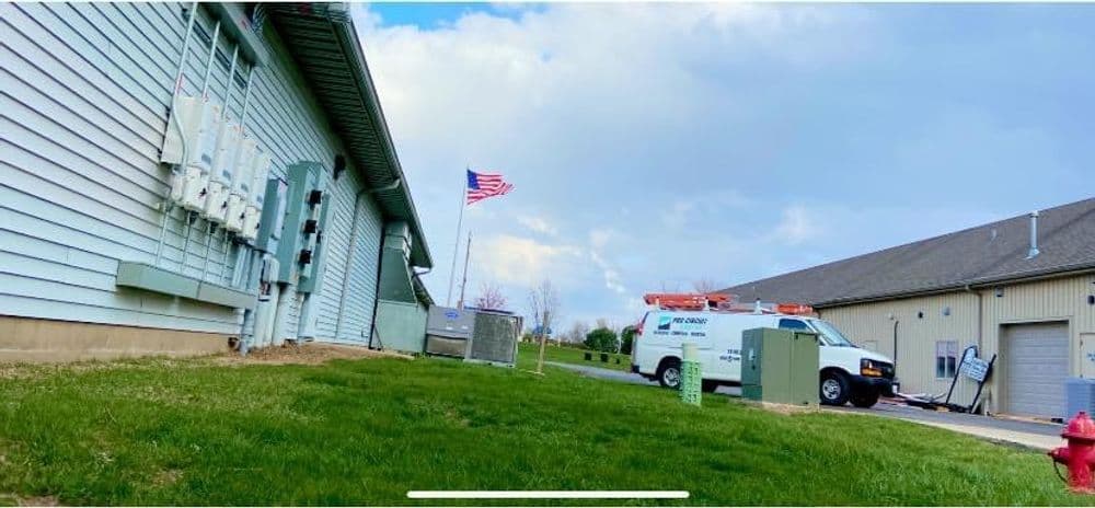 American flag waving near utility buildings with service vehicles on a grassy area.