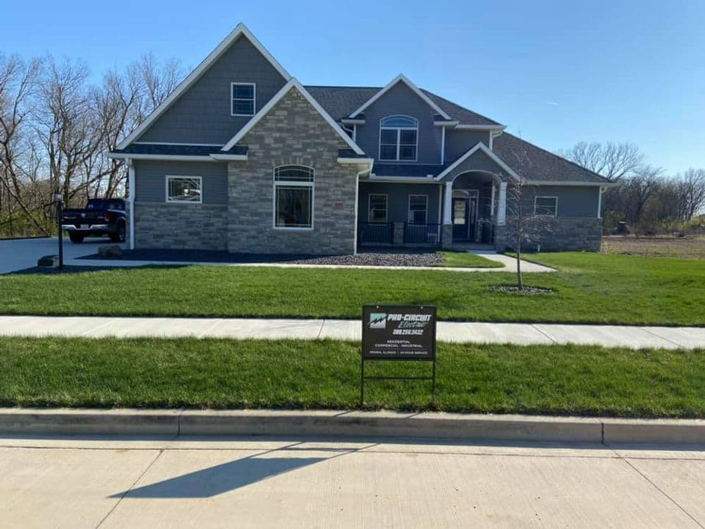 Modern two-story house with stone accents, front lawn, and sale sign.