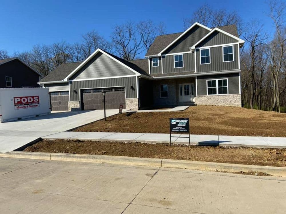 Newly constructed gray and stone house with garage, PODS container, and empty yard.