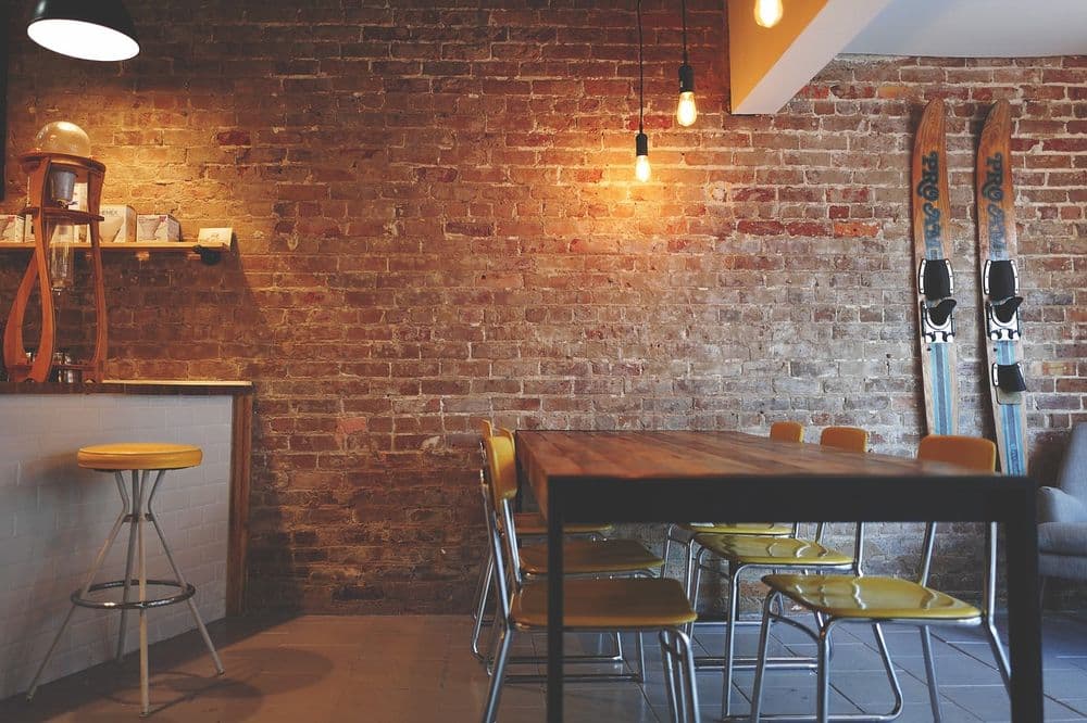 Cozy cafe interior with brick walls, wooden table, yellow chairs, and vintage skis decor.