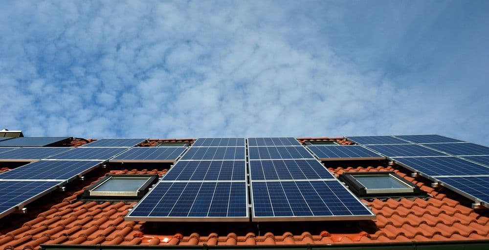 Solar panels installed on a red-tiled roof against a blue sky with scattered clouds.